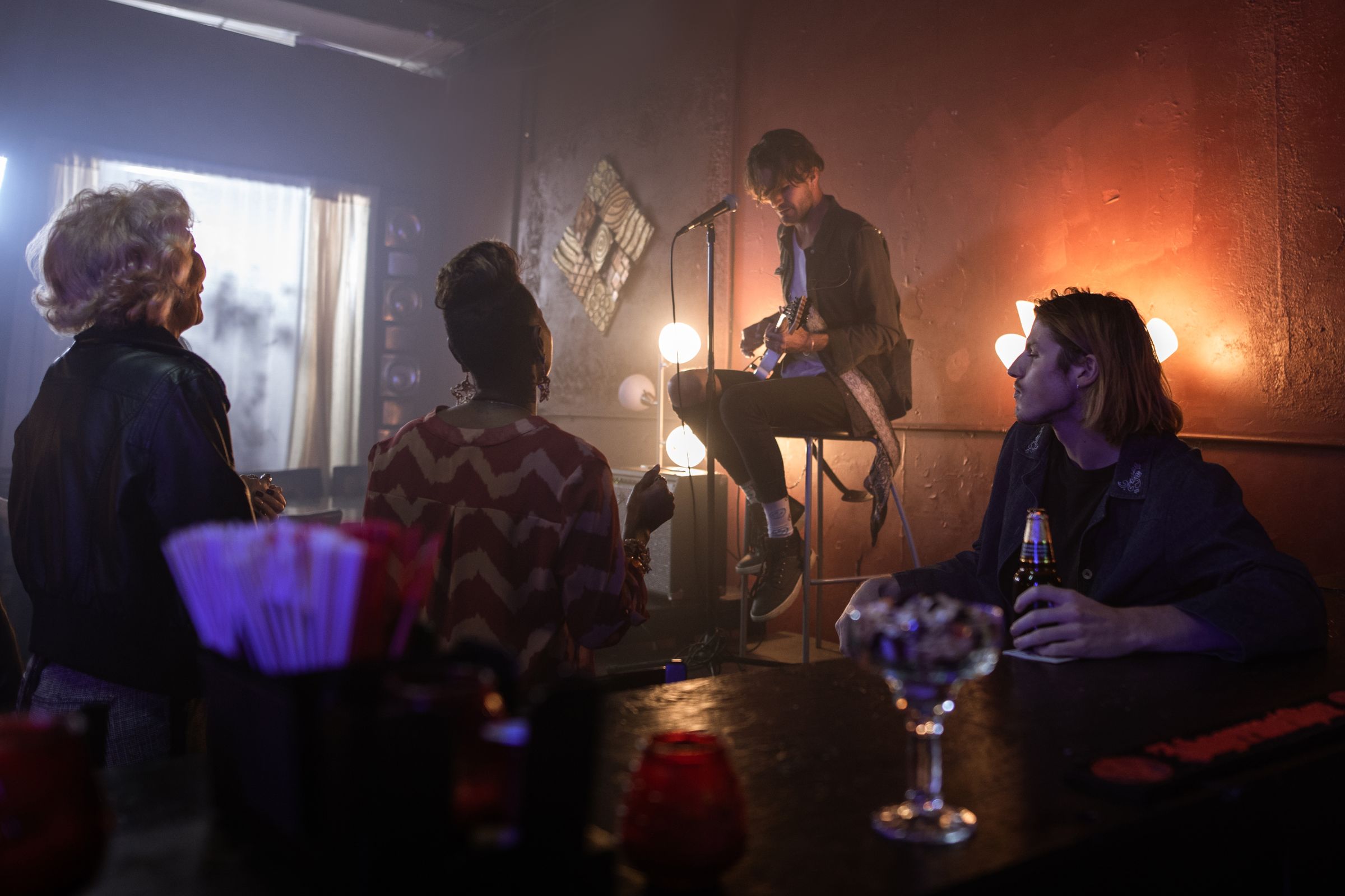 A seated acoustic guitarist performing for a few listeners in a small indoor venue; illustrative photography